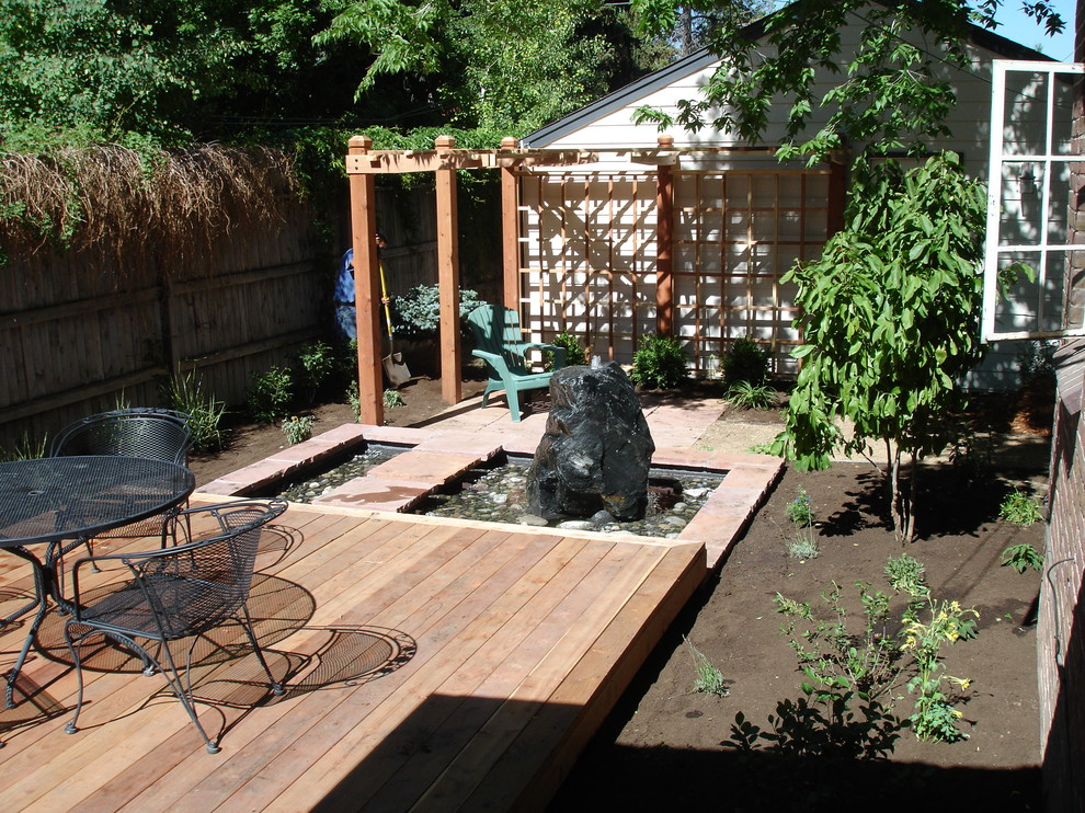 Ejemplo de jardín de estilo americano de tamaño medio en verano en patio trasero con fuente, exposición parcial al sol y entablado