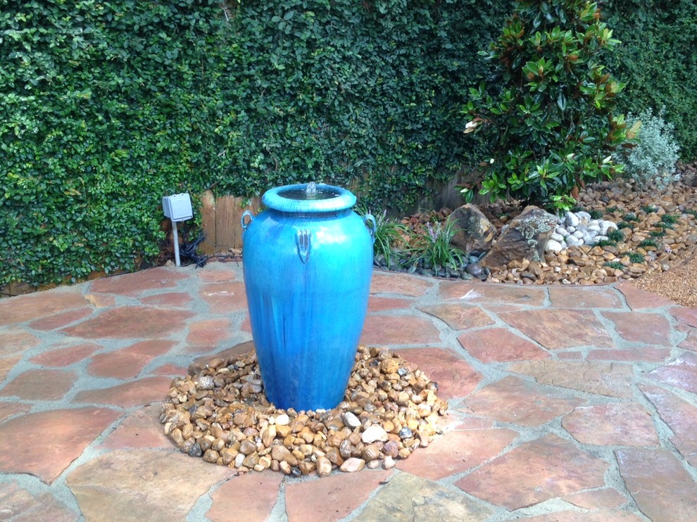 На фото: маленький садовый фонтан на склоне в стиле модернизм с полуденной тенью для на участке и в саду с