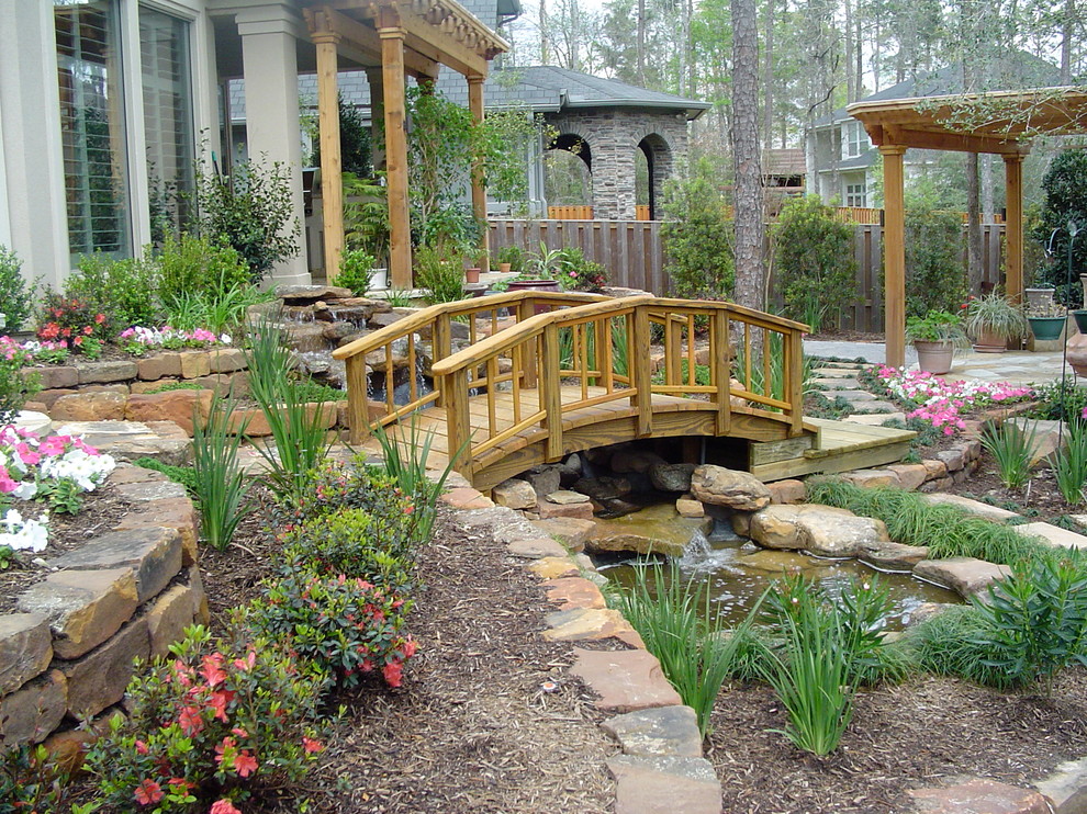 This is an example of a large traditional back partial sun garden for spring in Houston with a water feature and natural stone paving.