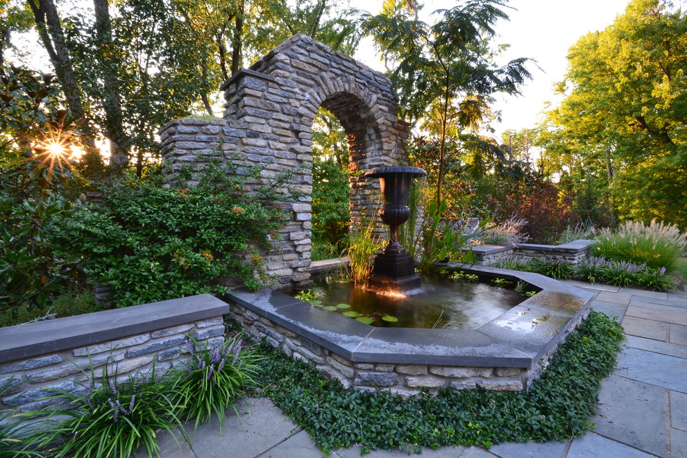 Imagen de jardín clásico grande en patio trasero con jardín francés, fuente, exposición parcial al sol y adoquines de piedra natural