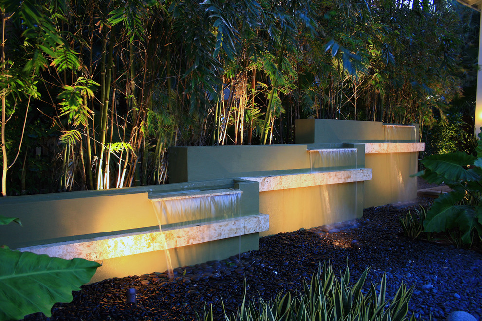 Ispirazione per un giardino tropicale di medie dimensioni e dietro casa con fontane e ghiaia