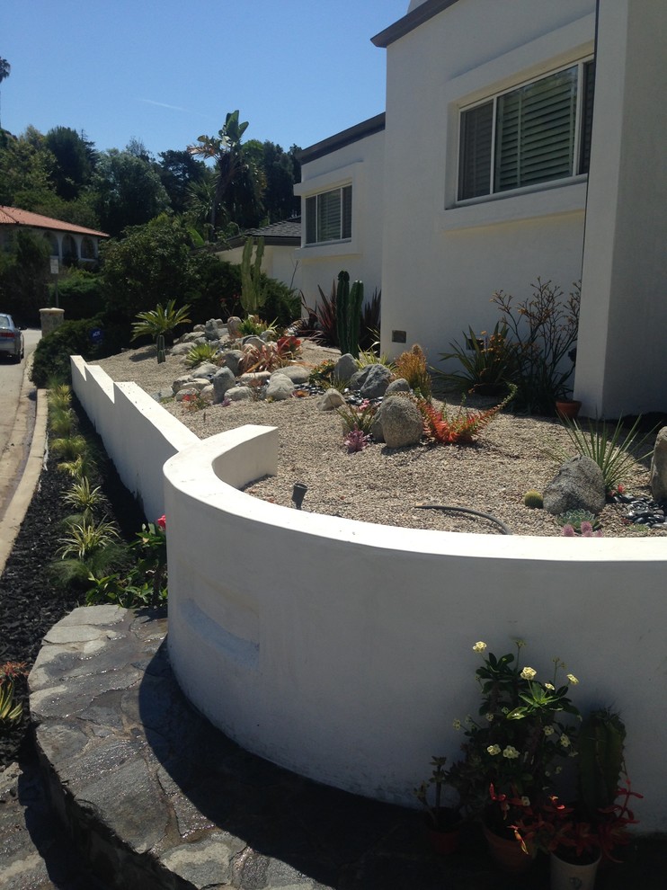 Ispirazione per un giardino xeriscape minimalista esposto a mezz'ombra di medie dimensioni e davanti casa con un muro di contenimento e ghiaia