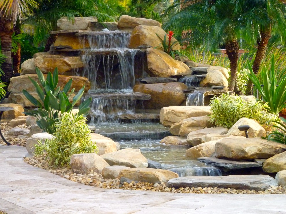 This is an example of a medium sized world-inspired back full sun garden in Miami with a water feature and natural stone paving.
