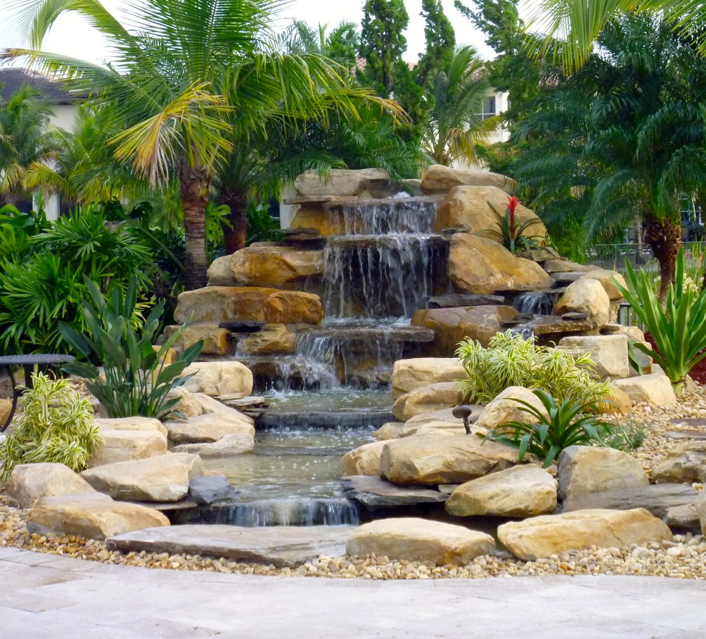 Mittelgroßer Gartenwasserfall hinter dem Haus mit direkter Sonneneinstrahlung und Natursteinplatten in Miami