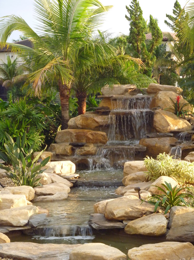 Foto på en mellanstor tropisk bakgård i full sol, med en fontän och naturstensplattor