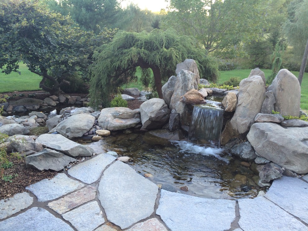 This is an example of a large rustic backyard stone water fountain landscape in Boston.