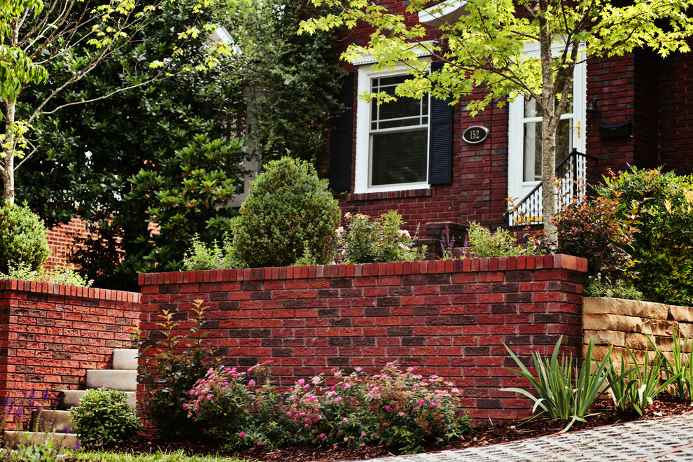 Small classic front full sun garden for summer in Charlotte with a retaining wall and brick paving.