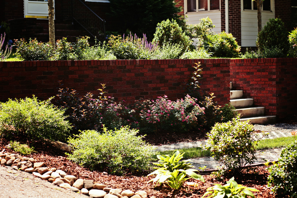 Immagine di un piccolo giardino eclettico esposto in pieno sole davanti casa in estate con un muro di contenimento e pavimentazioni in mattoni