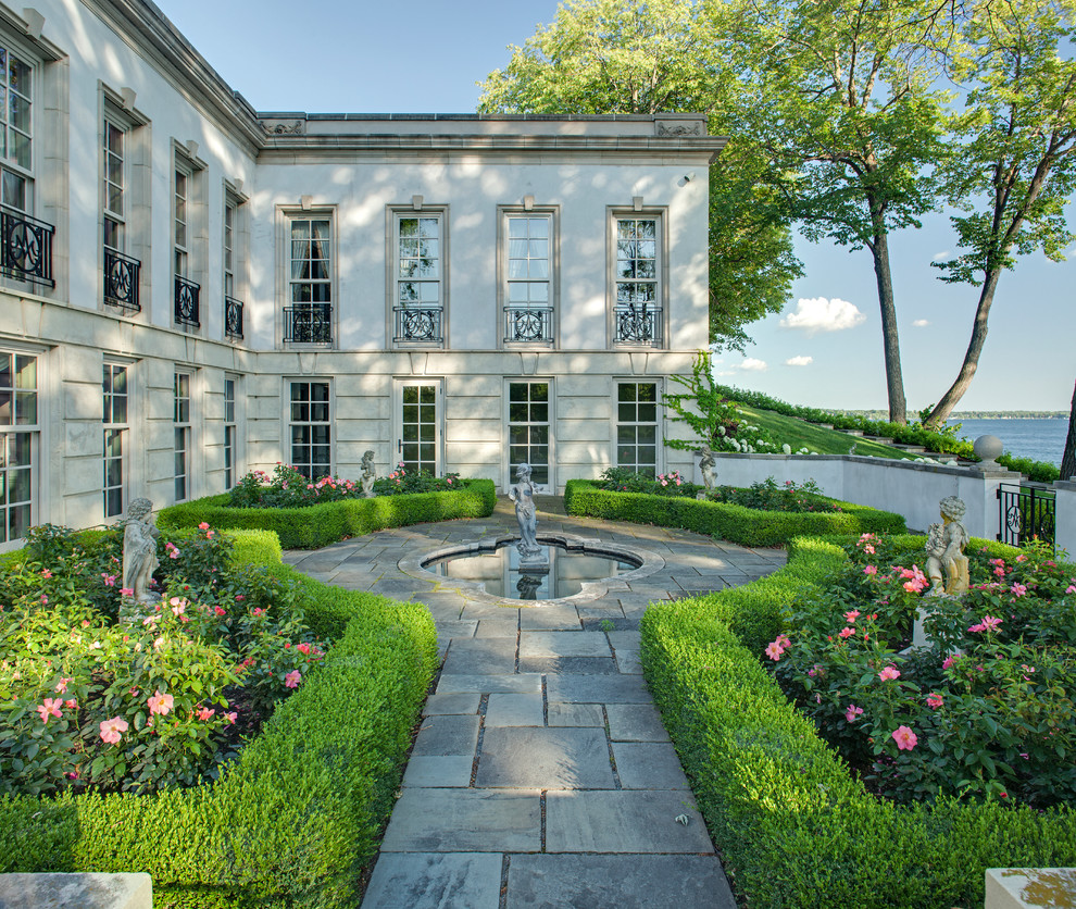 Modelo de jardín clásico en patio trasero con jardín francés, fuente y adoquines de piedra natural