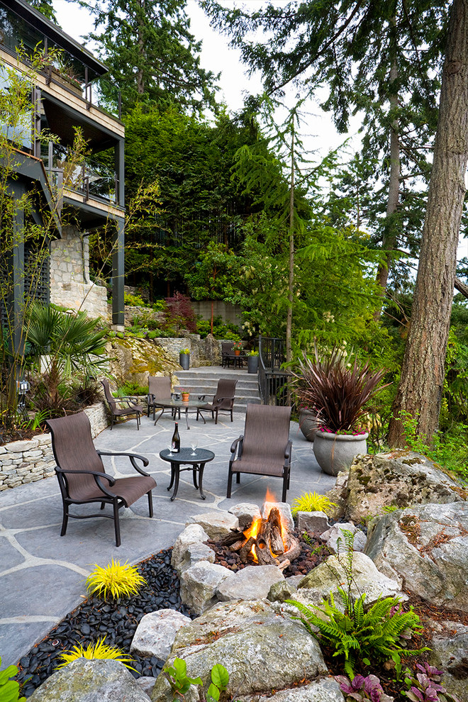 This is an example of a medium sized modern sloped partial sun garden for summer in Vancouver with a fire feature and natural stone paving.