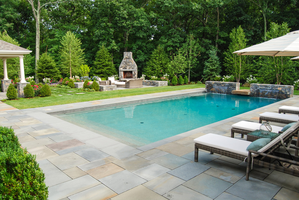 Modelo de piscina con fuente clásica grande en patio trasero con adoquines de piedra natural