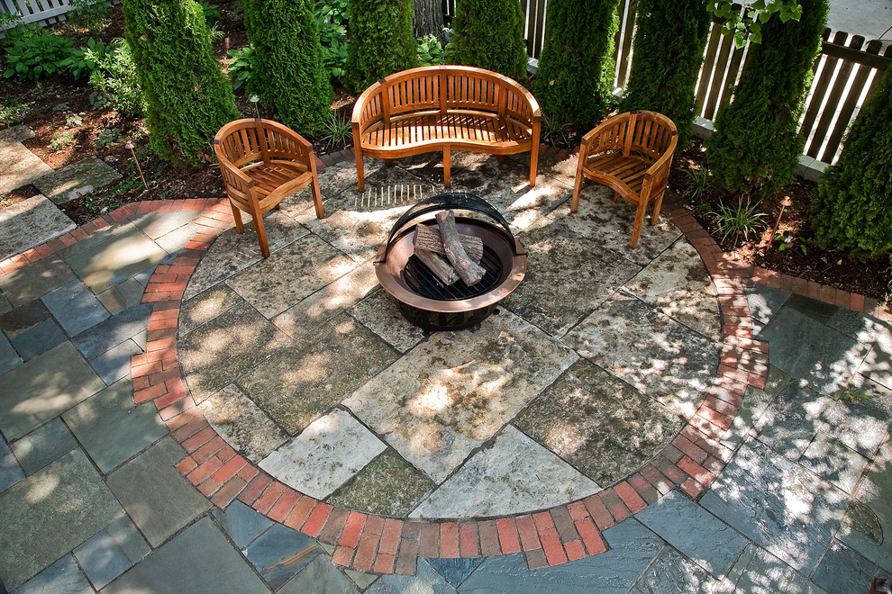 This is an example of a mid-sized traditional shade backyard stone landscaping in Milwaukee with a fire pit.