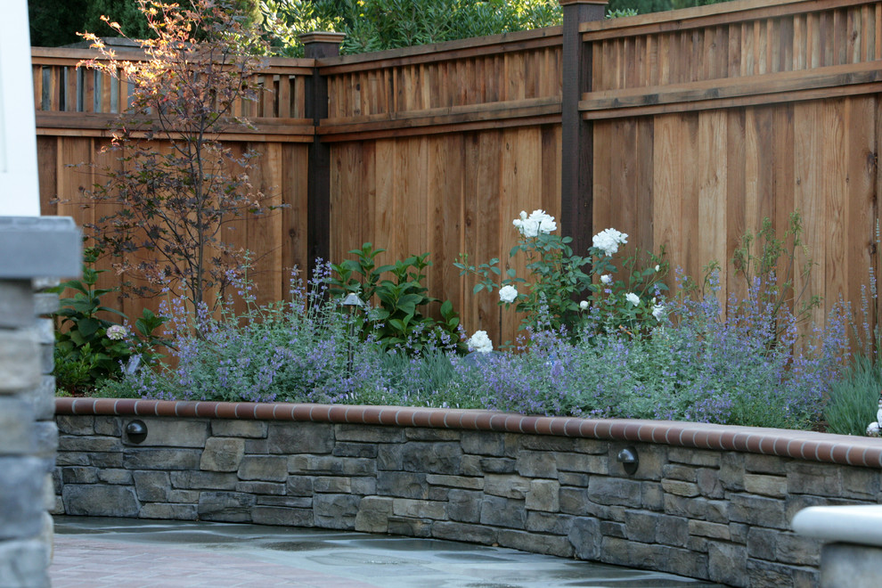 Cette image montre un grand jardin arrière traditionnel avec des pavés en pierre naturelle et un mur de soutènement.