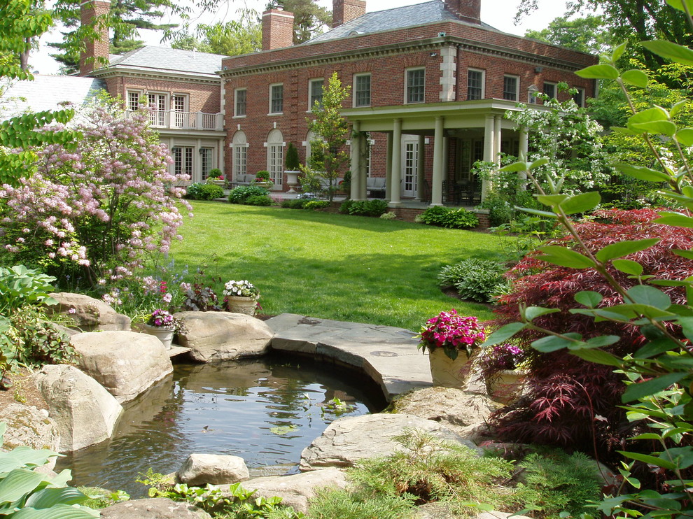 Imagen de jardín tradicional de tamaño medio en patio trasero con fuente, jardín francés, exposición parcial al sol y adoquines de piedra natural