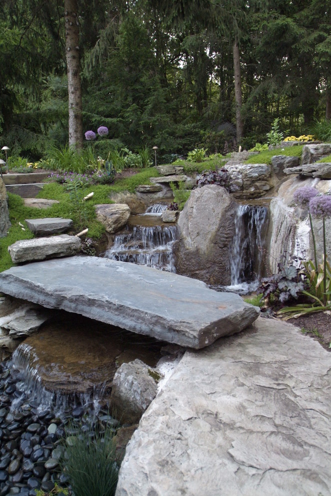 Cette image montre un grand jardin arrière traditionnel avec un bassin, une exposition partiellement ombragée et des pavés en pierre naturelle.