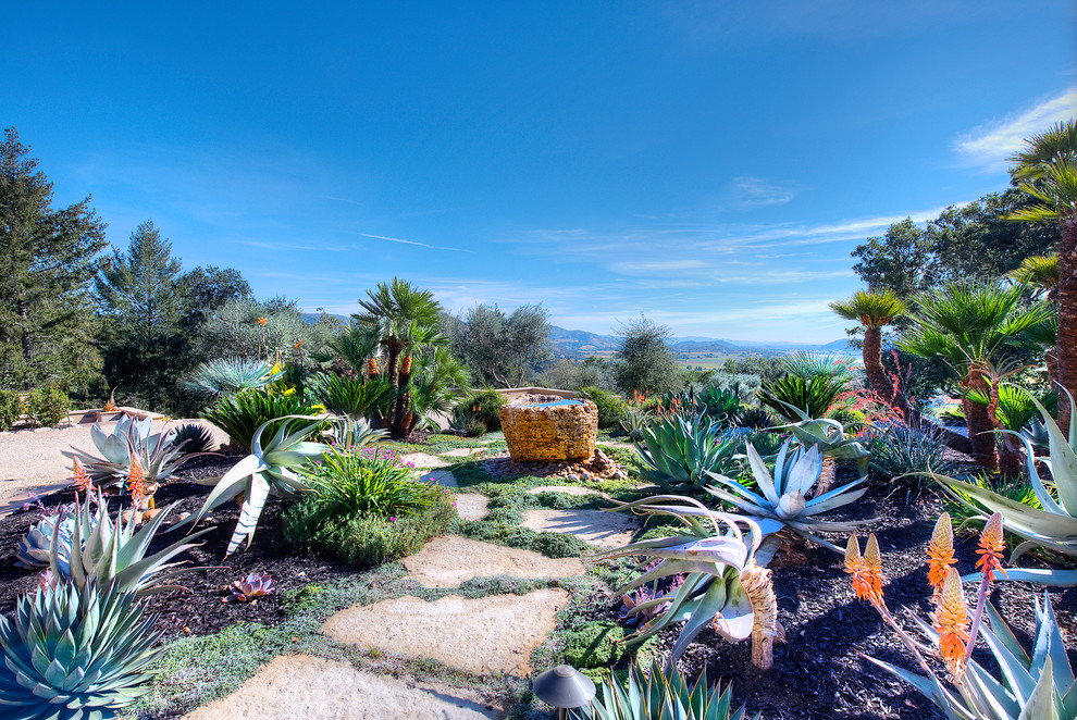 Immagine di un ampio giardino mediterraneo esposto in pieno sole davanti casa con fontane e pavimentazioni in pietra naturale