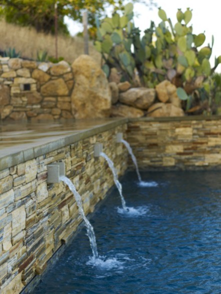 This is an example of a large mediterranean back partial sun garden in San Luis Obispo with a water feature and natural stone paving.