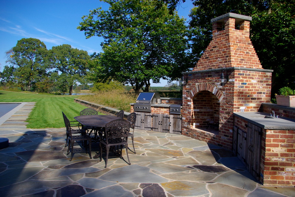 Immagine di un ampio patio o portico classico dietro casa con un focolare e pavimentazioni in pietra naturale
