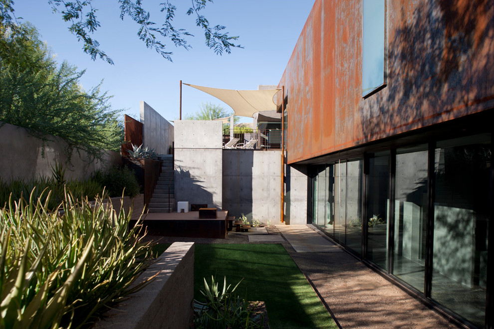 Photo of a medium sized modern back xeriscape partial sun garden for spring in Phoenix with a retaining wall and gravel.