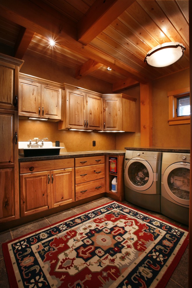 Rustik inredning av en stor tvättstuga enbart för tvätt, med luckor med upphöjd panel, skåp i mellenmörkt trä, granitbänkskiva, bruna väggar, klinkergolv i porslin, en tvättmaskin och torktumlare bredvid varandra och en nedsänkt diskho