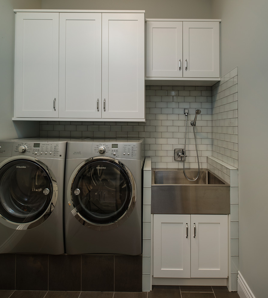 Inredning av en modern mellanstor linjär tvättstuga enbart för tvätt, med en allbänk, skåp i shakerstil, vita skåp, grå väggar, klinkergolv i keramik, en tvättmaskin och torktumlare bredvid varandra och grått golv