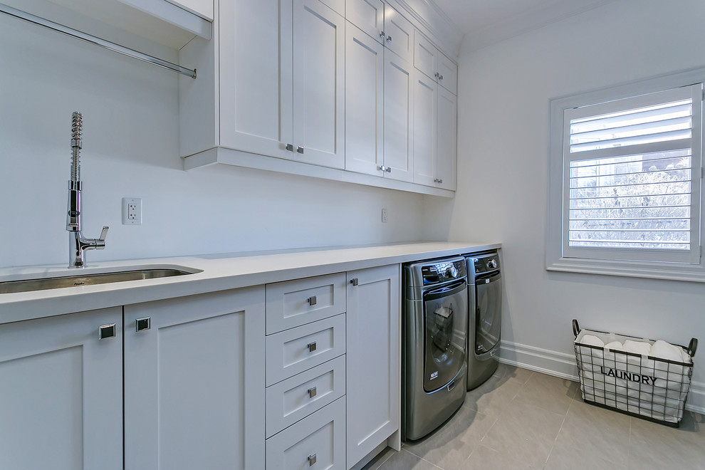 Photo of a large traditional single-wall utility room in Toronto with a submerged sink, shaker cabinets, white cabinets, engineered stone countertops, grey walls, ceramic flooring and a side by side washer and dryer.