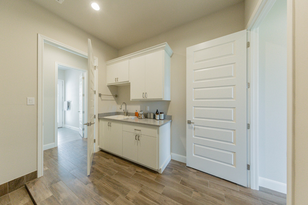 Photo of a large traditional separated utility room in Austin with a built-in sink, flat-panel cabinets, white cabinets, granite worktops, grey walls, porcelain flooring, a side by side washer and dryer and brown floors.