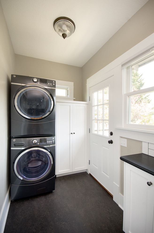 Example of a mid-sized transitional concrete floor dedicated laundry room design in Boise with recessed-panel cabinets, white cabinets, granite countertops, beige walls and a stacked washer/dryer