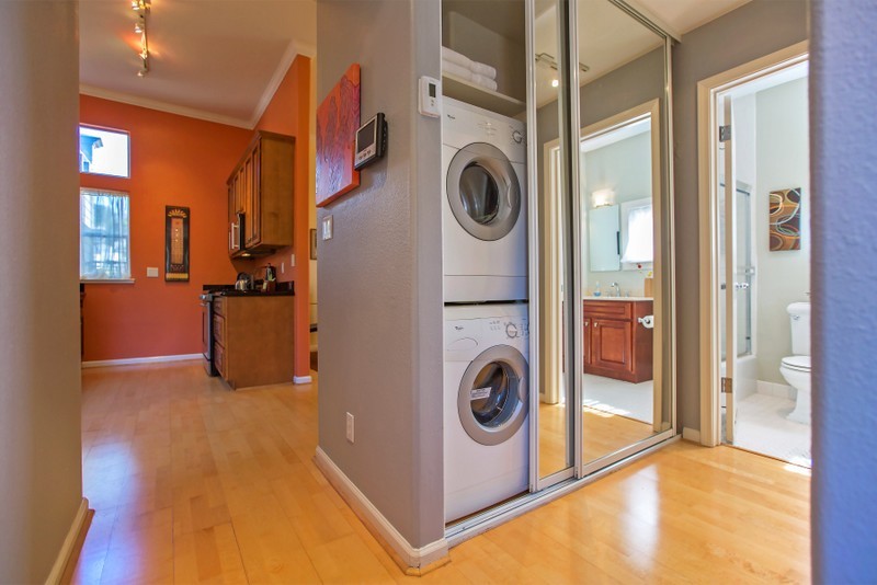 Kleiner, Einzeiliger Moderner Hauswirtschaftsraum mit Waschmaschinenschrank, Waschmaschine und Trockner gestapelt, grauer Wandfarbe und Bambusparkett in San Francisco