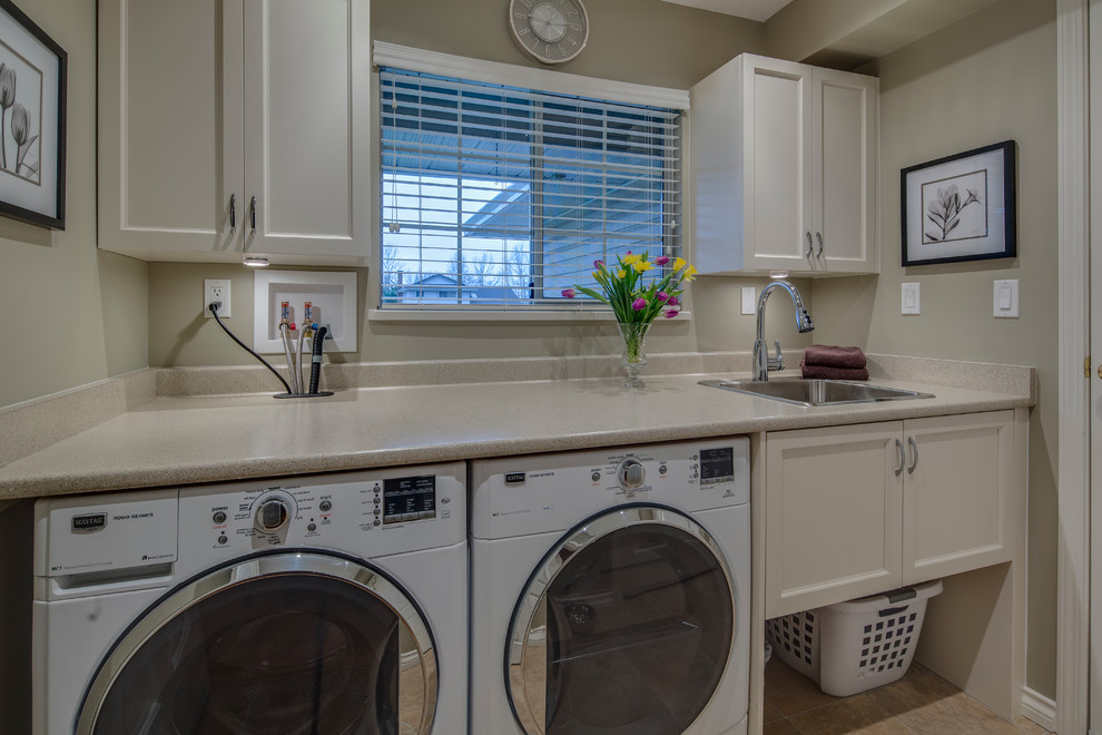 Ejemplo de cuarto de lavado lineal clásico grande con fregadero encastrado, armarios estilo shaker, puertas de armario blancas, suelo de baldosas de porcelana, lavadora y secadora juntas y paredes grises