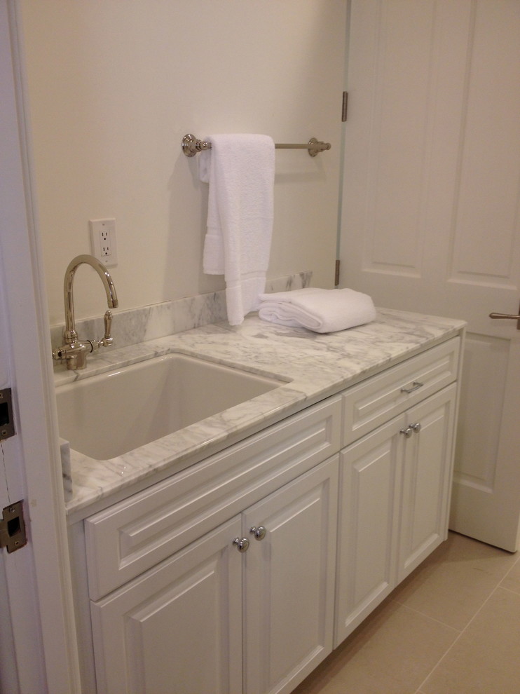 Exempel på en mellanstor klassisk parallell tvättstuga enbart för tvätt, med luckor med upphöjd panel, vita skåp, marmorbänkskiva, en tvättmaskin och torktumlare bredvid varandra, en allbänk, vita väggar och klinkergolv i porslin