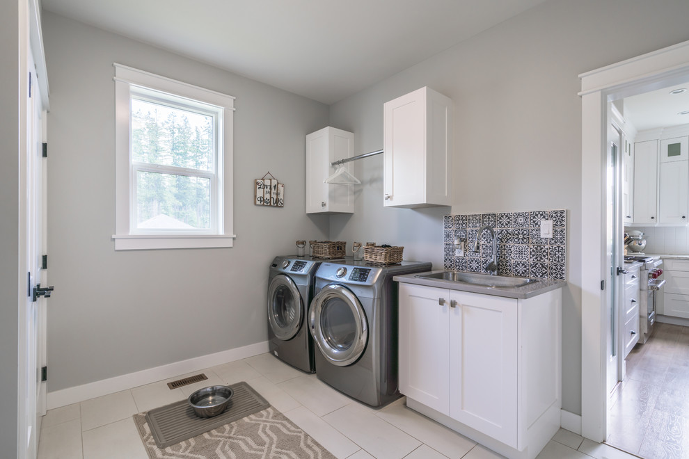 Idéer för mellanstora funkis linjära grått tvättstugor enbart för tvätt, med en nedsänkt diskho, skåp i shakerstil, vita skåp, grå väggar, en tvättmaskin och torktumlare bredvid varandra och vitt golv