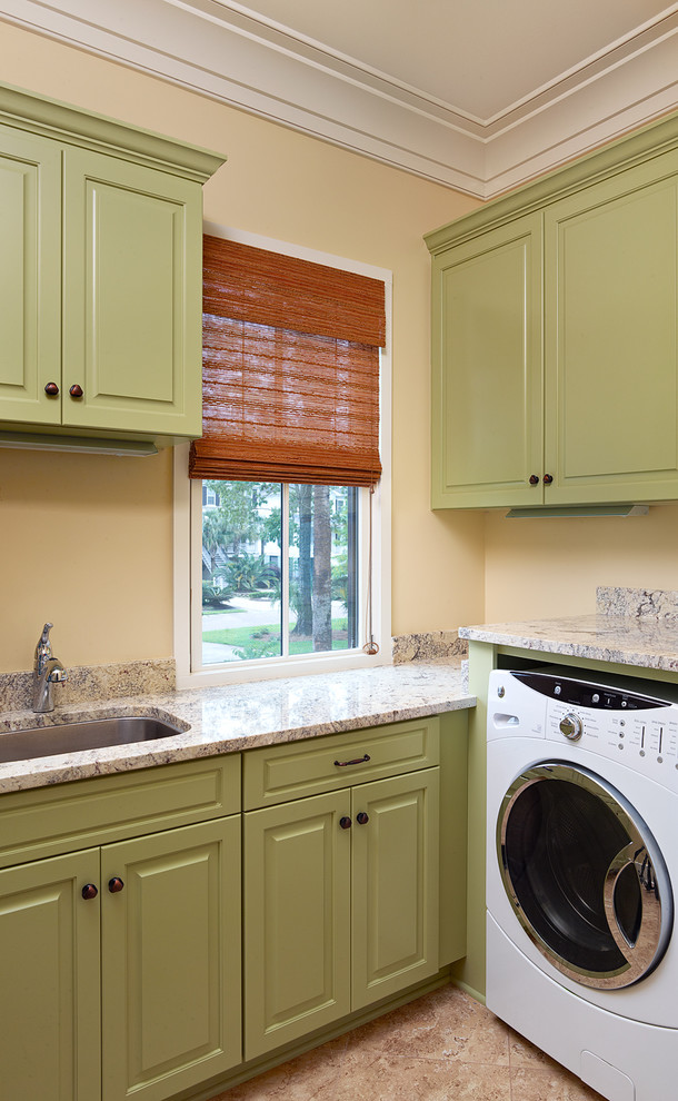 Klassische Waschküche in L-Form mit Unterbauwaschbecken, Waschmaschine und Trockner nebeneinander, Granit-Arbeitsplatte, grünen Schränken, profilierten Schrankfronten und Porzellan-Bodenfliesen in Charleston