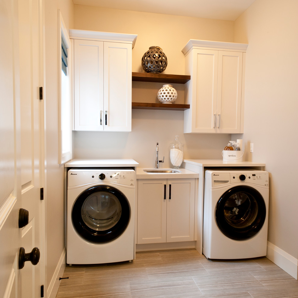 Inredning av en klassisk vita linjär vitt tvättstuga enbart för tvätt, med en undermonterad diskho, skåp i shakerstil, vita skåp, beige väggar, ljust trägolv, en tvättmaskin och torktumlare bredvid varandra och brunt golv
