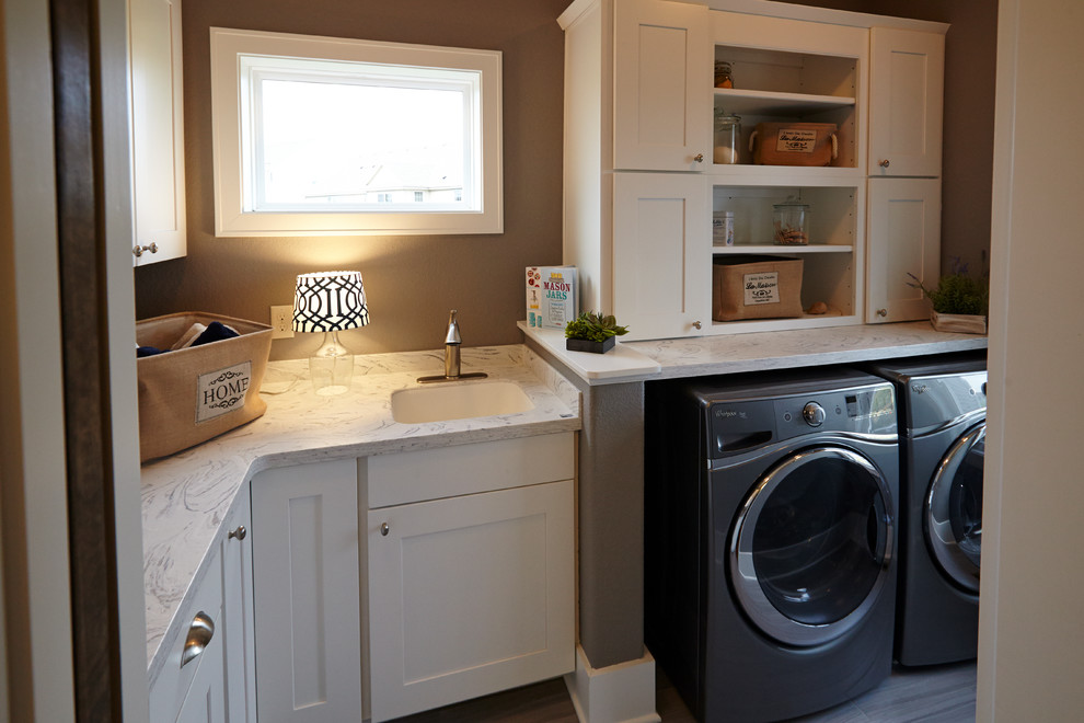Bild på en mellanstor vintage l-formad tvättstuga enbart för tvätt, med en enkel diskho, luckor med infälld panel, vita skåp, grå väggar, klinkergolv i keramik och en tvättmaskin och torktumlare bredvid varandra