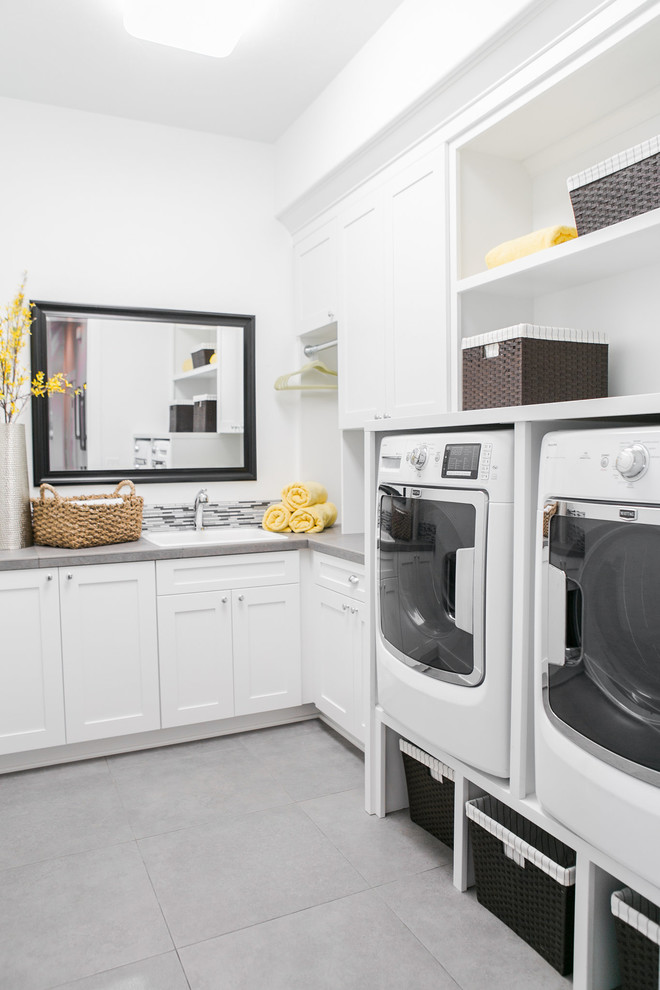 Modelo de lavadero en L tradicional renovado con fregadero encastrado, armarios estilo shaker, puertas de armario blancas, paredes blancas, lavadora y secadora juntas y encimeras grises