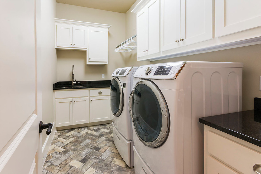Ejemplo de cuarto de lavado en L clásico renovado de tamaño medio con fregadero bajoencimera, armarios estilo shaker, puertas de armario blancas, paredes beige, suelo de ladrillo y lavadora y secadora juntas