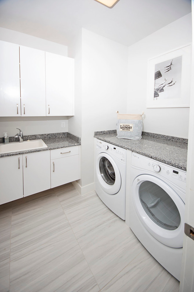 Große Moderne Waschküche in L-Form mit Unterbauwaschbecken, flächenbündigen Schrankfronten, weißen Schränken, Granit-Arbeitsplatte, weißer Wandfarbe, Marmorboden und Waschmaschine und Trockner nebeneinander in Miami