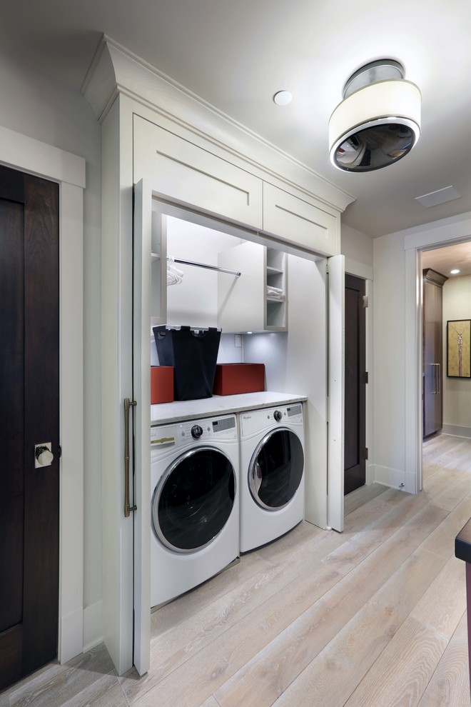 This is an example of a small modern single-wall laundry cupboard with open cabinets, white cabinets, marble worktops, white walls, light hardwood flooring, a side by side washer and dryer and brown floors.