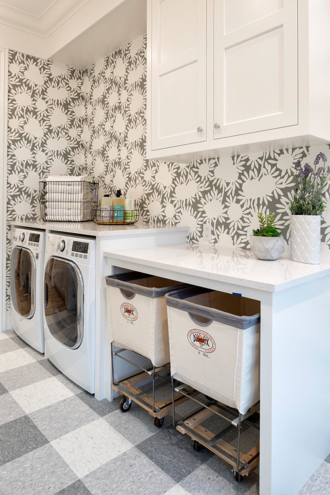 Klassisk inredning av en vita linjär vitt tvättstuga, med skåp i shakerstil, vita skåp, flerfärgade väggar, en tvättmaskin och torktumlare bredvid varandra och grått golv