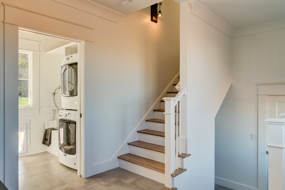 Inspiration for a small country galley utility room in Other with white cabinets, white walls, ceramic flooring, a stacked washer and dryer and grey floors.