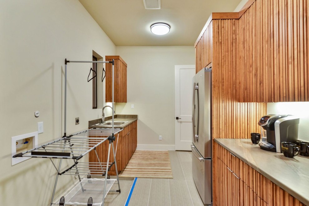 Large contemporary l-shaped separated utility room in Austin with a built-in sink, flat-panel cabinets, medium wood cabinets, composite countertops, beige walls, laminate floors and beige floors.