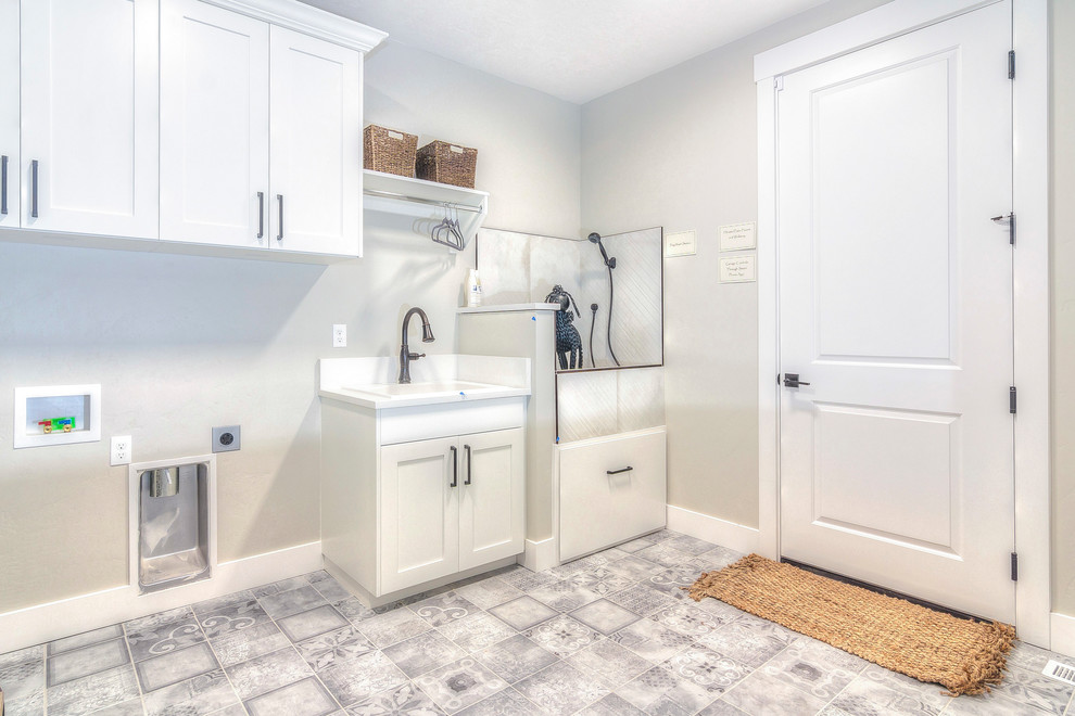 ボイシにある高級な中くらいなトラディショナルスタイルのおしゃれな家事室 (I型、ドロップインシンク、落し込みパネル扉のキャビネット、白いキャビネット、クオーツストーンカウンター、グレーの壁、セラミックタイルの床、左右配置の洗濯機・乾燥機、グレーの床、白いキッチンカウンター) の写真