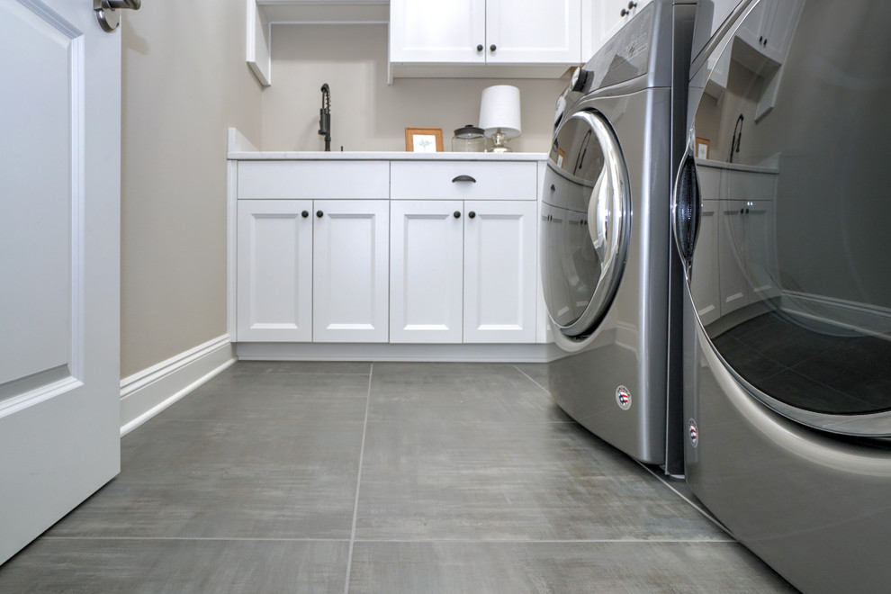 Idéer för mellanstora vintage l-formade vitt tvättstugor enbart för tvätt, med en undermonterad diskho, luckor med infälld panel, vita skåp, grå väggar, en tvättmaskin och torktumlare bredvid varandra och grått golv