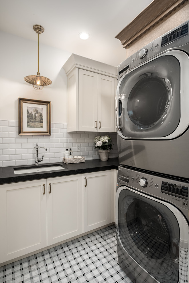 Idéer för lantliga l-formade svart tvättstugor enbart för tvätt, med en undermonterad diskho, skåp i shakerstil, vita skåp, vita väggar, en tvättmaskin och torktumlare bredvid varandra och flerfärgat golv