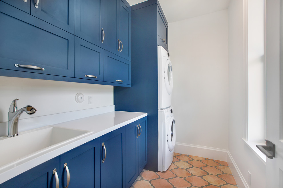 Bild på en mellanstor 50 tals parallell tvättstuga enbart för tvätt, med en allbänk, skåp i shakerstil, blå skåp, vita väggar, klinkergolv i terrakotta och en tvättpelare