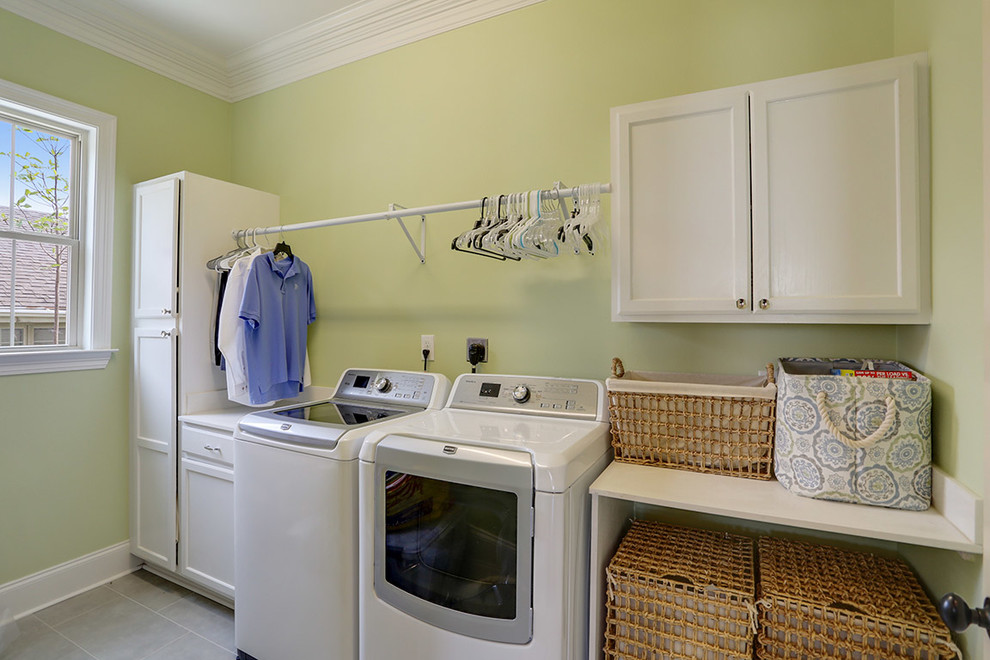 Mittelgroße Klassische Waschküche mit flächenbündigen Schrankfronten, weißen Schränken, Arbeitsplatte aus Holz, gelber Wandfarbe, Keramikboden und Waschmaschine und Trockner nebeneinander in New Orleans