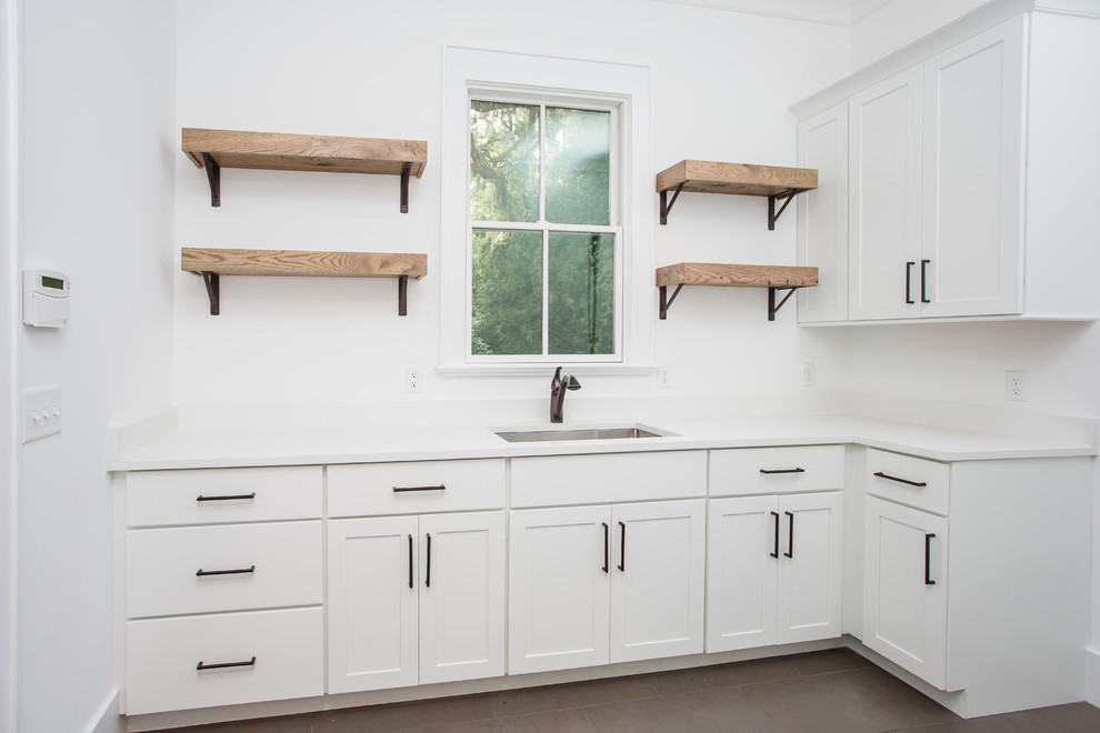 Inspiration for a mid-sized country l-shaped brown floor dedicated laundry room remodel in Jacksonville with an undermount sink, shaker cabinets, white cabinets, solid surface countertops and white walls
