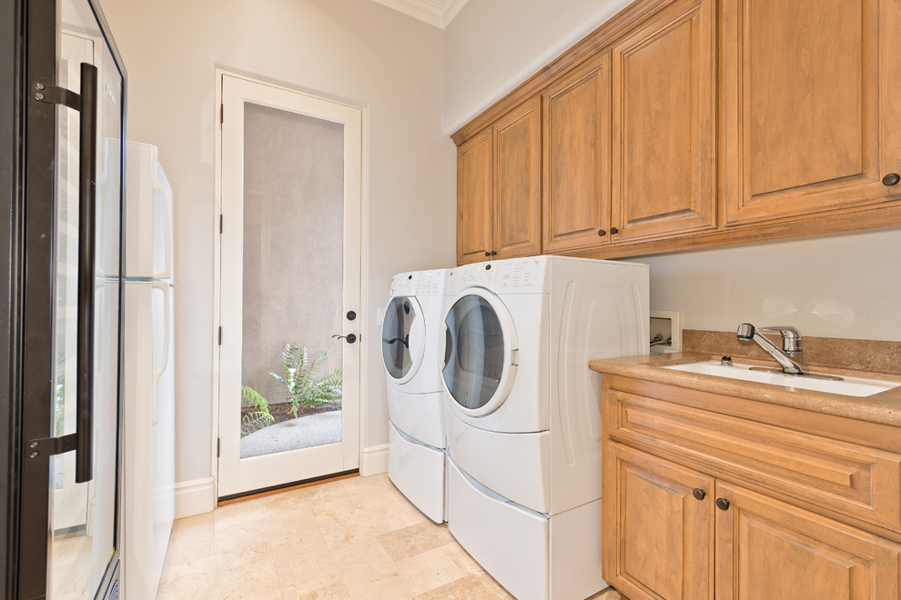 Inspiration for a medium sized retro single-wall utility room in San Diego with a submerged sink, raised-panel cabinets, medium wood cabinets, granite worktops, grey walls, travertine flooring and a side by side washer and dryer.