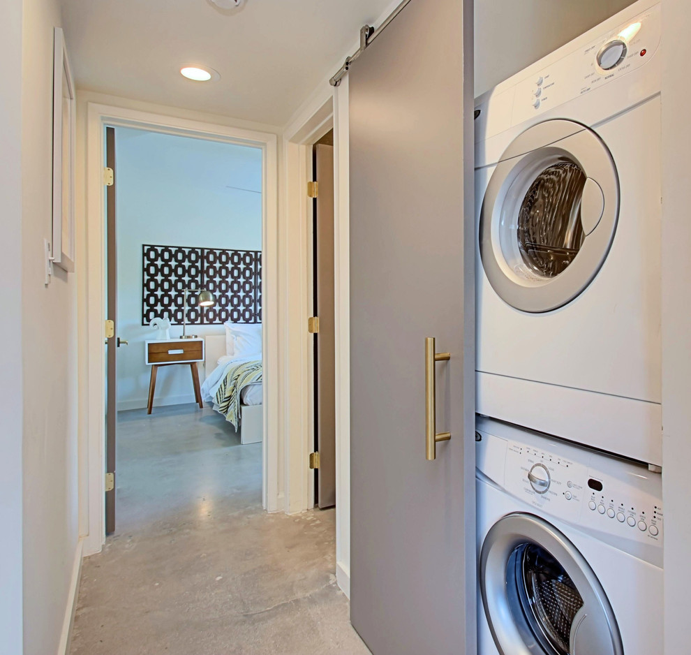 Esempio di un piccolo ripostiglio-lavanderia moderno con pareti bianche, pavimento in cemento e lavatrice e asciugatrice a colonna